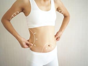 Slender woman with sculpted body reclines in chair, happy with her body after surgical body contouring